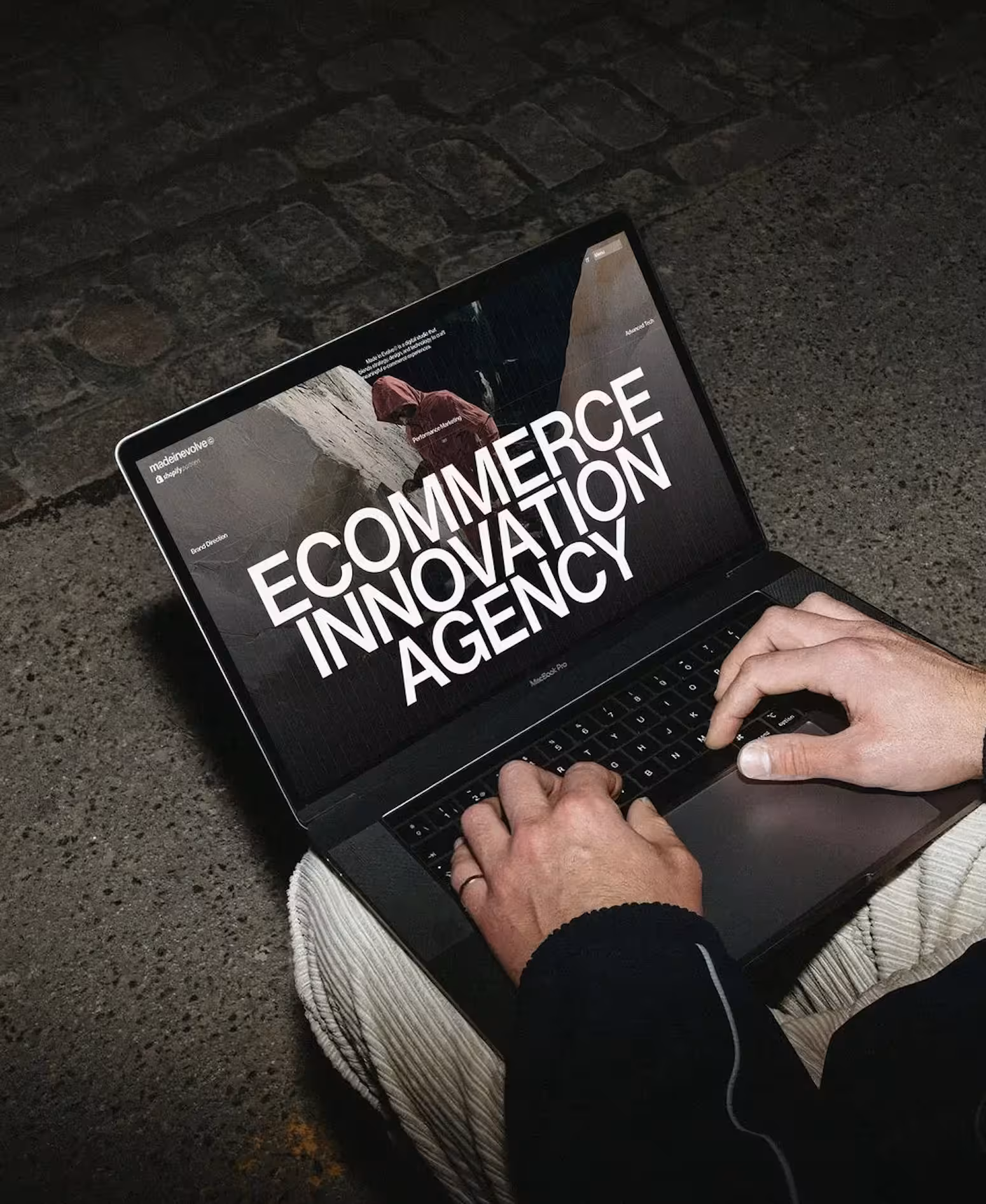 Person typing on MacBook Pro showing screen with text 'ECOMMERCE INNOVATION AGENCY'.
