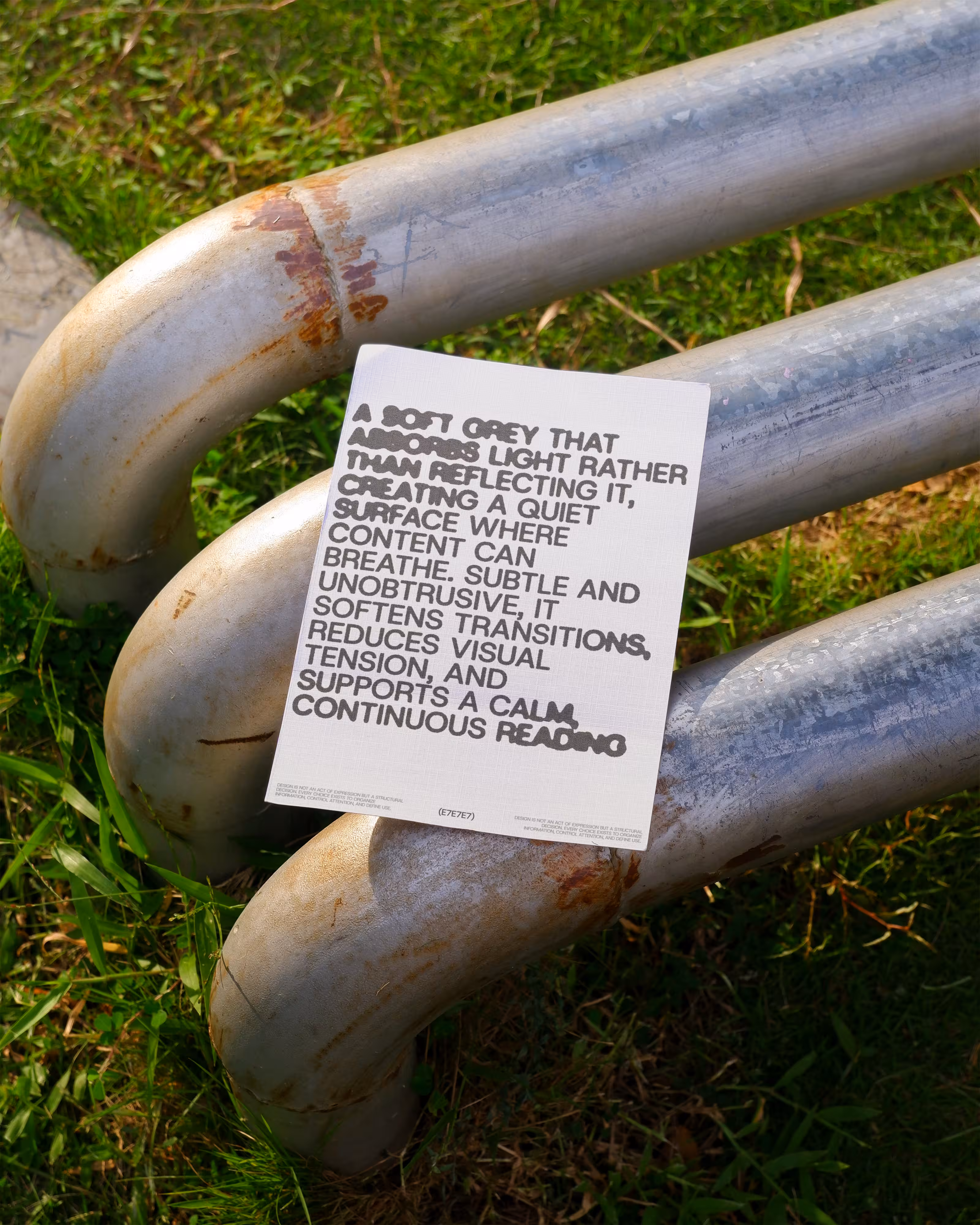 A card with text about soft grey on three rusted metal pipes on grass.