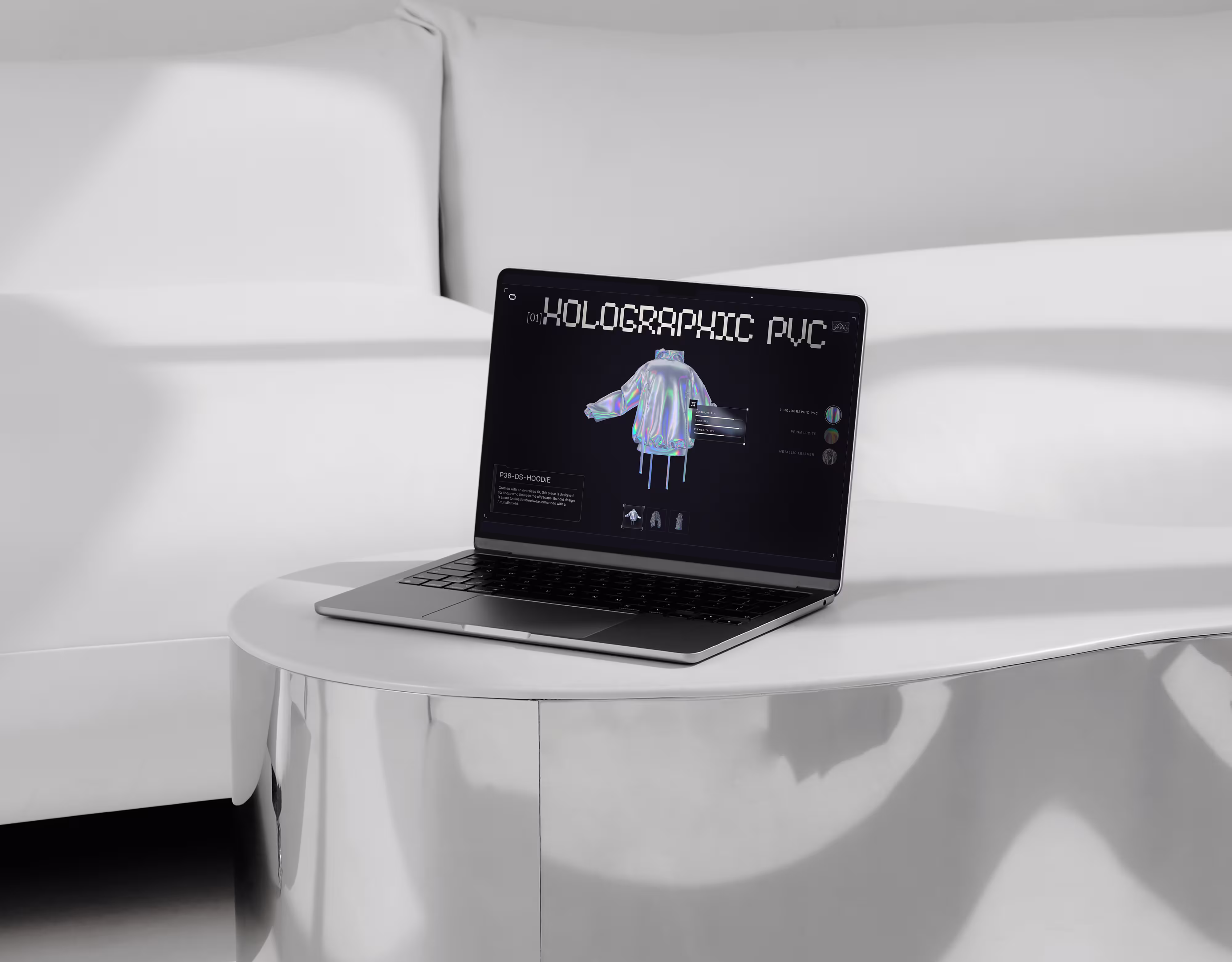 Laptop on white table shows holographic PVC hoodie design on screen in a monochrome room.